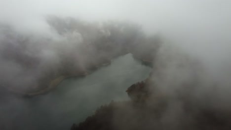 Aerial-flight-through-rain-clouds-over-remote,-tranquil-mountain-lake