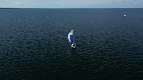A-sailboat-gracefully-sails-the-Baltic-Sea-with-a-colorful-gennaker-sail,-seen-from-behind,-drone-perspective,-a-few-islands-on-the-horizon