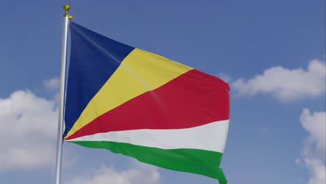 Bandera-De-Seychelles-Moviéndose-En-El-Viento-Con-Un-Cielo-Azul-Claro-En-El-Fondo,-Nubes-Moviéndose-Lentamente,-Asta-De-Bandera,-Cámara-Lenta