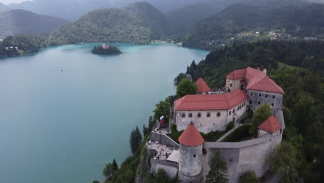 Castillo-De-Sobrevuelo-Aéreo-En-La-Colina-Y-La-Famosa-Isla-Con-Iglesia-En-El-Lago-En-Bled,-Eslovenia