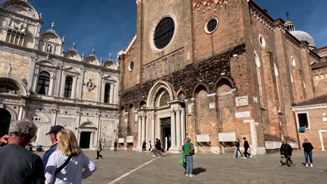 San-Zanipolo-Church-And-Scuola-Grande-di-San-Marco-With-Tourists-Walking-Past-The-Piazza-In-Venice