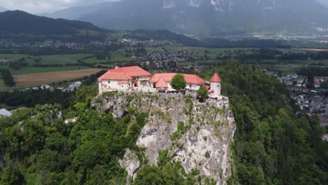 Aerial-tilt-up-shot-of-famous-castle-in-Bled-during-sunny-day-and-mountains-in-background
