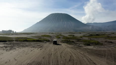 Flying-over-a-desert-truck,-driving-toward-the-Bromo-mountain,-in-Java,-Indonesia---Aerial-view