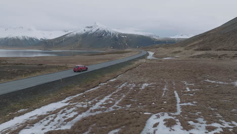 Tracking-Drone-Shot-of-Red-Car-Moving-on-Road-in-Cold-Landscape-of-Iceland