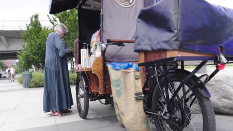 An-elderly-woman-buys-coffee-at-a-street-mobile-stand-on-the-waterfront