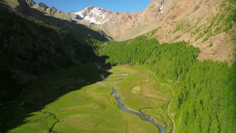 Predarossa-plain-and-Duino-river-flowing-in-summer-season-in-Val-Masino-with-mountains-in-background,-Italy