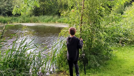 4K-60FPS-Boy-is-Trying-to-Get-Fishing-Tackle-Down-From-Tree-Under-Fishing-in-a-Beautiful-Pond-in-Denmark