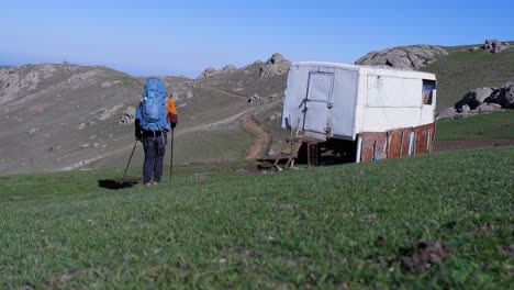 Backpack-hiker-walks-past-travel-trailer-bunkhouse-on-mtn-hillside