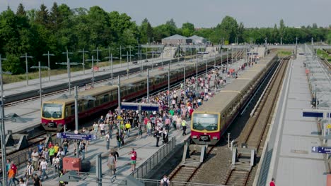 Belebter-Bahnhof-Im-Freien,-überfüllte-Bahnsteige,-Züge-Auf-Gleisen-Unter-Blauem-Himmel,-Eingerahmt-Von-Bäumen-Und-Gebäuden