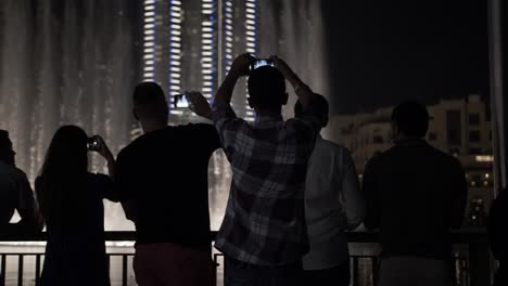 Tourists,-people-watching-the-water-fountain,-light-show-and-taking-pictures-with-phones-at-the-Dubai-mall