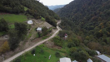 Aerial-follows-dirt-road-out-of-village-on-steep-forest-mountain-slope