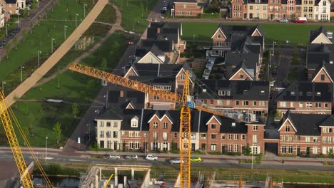 Medium-aerial-orbiting-view-of-a-yellow-tower-crane-building-a-new-housing-development-in-teh-town-of-Weesp-near-Amsterdam,-Netherlands