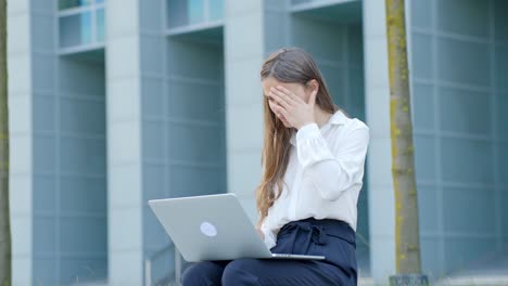 Worried-corporate-woman-with-laptop-outside-modern-office,-typing