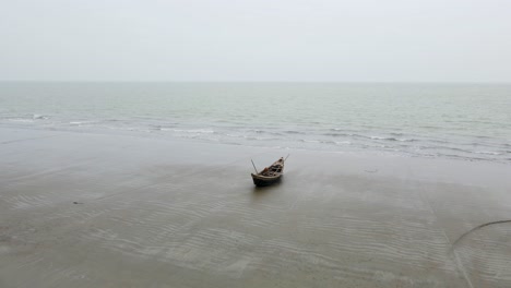 In-Dieser-Langsamen-Drohnenaufnahme-Ruht-Ein-Einzelnes-Bootskanu-Am-Ufer-Des-Strandes-Bei-Ebbe-In-Bangladesch