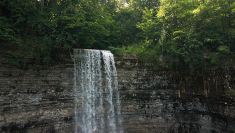 Pullback-from-top-of-ribbon-waterfall-of-tew-falls-with-layered-sedimentary-rock-cliff