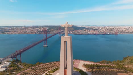 Orbit-Shot-Of-Christ-Statue-And-Suspended-Bridge-Over-Blue-Seascape,-Lisbon,-Portugal