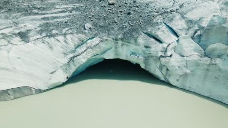 Giant-Ice-Cave-in-a-Glacier-Melting-in-a-lake-below-due-to-Climate-Change-in-the-Alps,-view-from-above