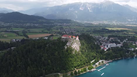 Aerial-view-of-castle-on-hill,-with-port-and-mountain-range-of-Slovenia-in-background