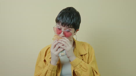 Modern-short-haired-woman-voraciously-chomping-a-burger-in-a-studio-background