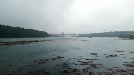 Misty-blue-coloured-overcast-Menai-Straits-Britannia-bridge-crossing-into-Anglesey,-Wales
