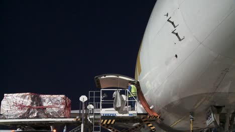 Airport-worker-lifts-up-cargo-container-goods-and-loads-airplane-at-night