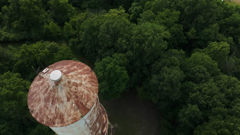 Overhead-aerial-shot-of-old-rusty-roof-of-water-tower-surrounded-by-trees
