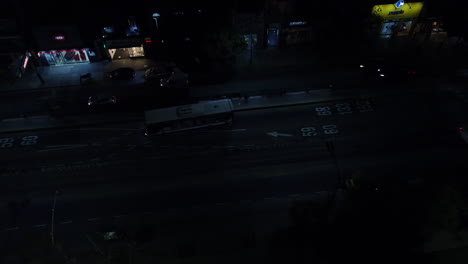 Bus-stop-at-night-in-Buenos-Aires,-the-bus-leaves-the-stop,-people-are-waiting-for-the-next-bus,-drone-footage