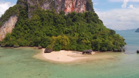 Aerial-Drone-View-Rai-Island-Beach-in-Thailand-with-a-Secluded-Couple-Walking-Down-the-Beach,-near-Hong-Island,-Phuket,-Krabi---Beautiful-Turquoise-Sea-Water,-Sand,-Lush-Green-Trees,-Blue-Sky,-Cliff