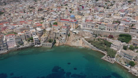 Aerial:-Slow-backwards-reveal-shot-of-Asteria-Beach-in-Ermoupoli-of-Syros-island,-Greece-during-sunrise