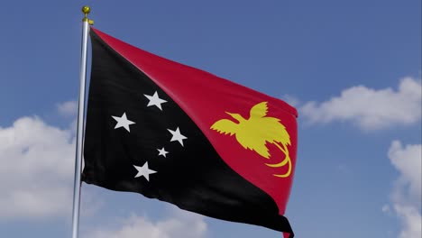 Bandera-De-Papúa-Nueva-Guinea-Moviéndose-En-El-Viento-Con-Un-Cielo-Azul-Claro-En-El-Fondo,-Nubes-Moviéndose-Lentamente,-Asta-De-Bandera,-Cámara-Lenta