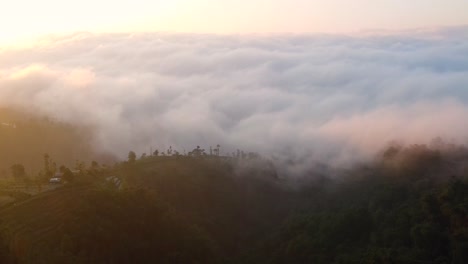 Luftaufnahme-Eines-überwucherten-Berges-Und-Einer-Dichten-Wolkenlandschaft,-Die-Das-Tal-In-Indonesien-Während-Des-Goldenen-Sonnenaufgangs-Versteckt