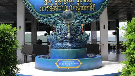 Thai-Chinese-Temple-Signage-with-Blue-Mosaic-Design,-Statue,-and-Lush-Surroundings