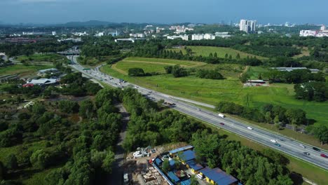 City-suburbs-and-highway-road-with-green-meadows-around,-aerial-view