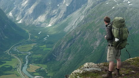 Excursionista-Masculino-Parado-En-El-Borde-De-Una-Impresionante-Cresta-En-Noruega,-Romdalseggen,-Hombre-Disfrutando-De-La-Vista-En-Las-Montañas