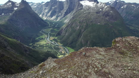 Two-Hikers-Walking-Away-from-the-Edge-of-a-Stunning-Breathtaking-Ridge-in-Norway,-Romdalseggen,-Aerial-View
