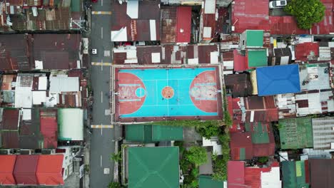 Top-down-aerial-view-of-local-youth-playing-at-a-basketball-court-in-impoverished-area-of-West-Crame,-Quezon-City,-Philippines