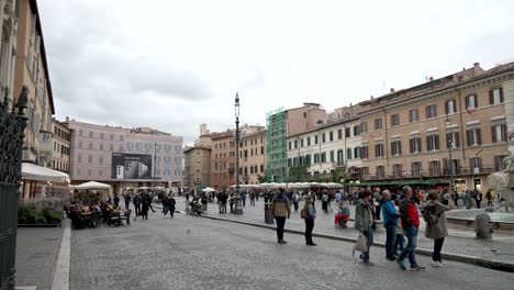 Touristen,-Die-An-Einem-Bewölkten,-Bewölkten-Tag-über-Die-Piazza-Navona-In-Rom-Spazieren,-Mit-Einem-Straßencafé-Im-Hintergrund