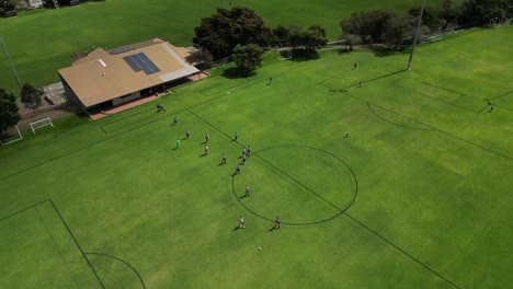 Aerial-top-down-showing-teams-entering-grass-field-of-Amateur-Soccer-Stadium-in-Australia---Orbiting-shot