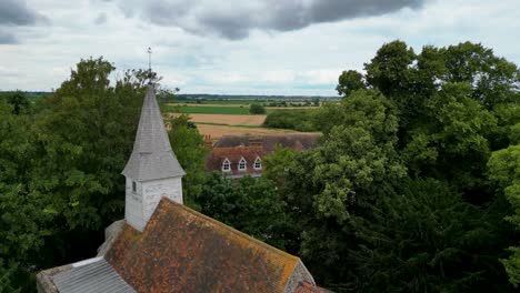 A-quick-rising-boom-shot-of-All-Saints-church-in-West-Stourmouth,-rising-to-show-the-fields-behind