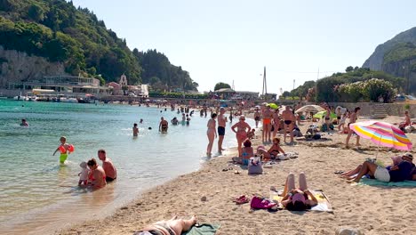 People-at-the-Beach-Swimming-and-Sunbathing,-Windy-weather-in-Palaiokastritsa-Corfu-Greece,-Real-Time-Footage