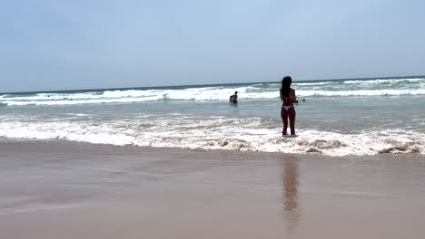 In-Caparica,-a-fit-woman-in-a-bikini-elegantly-wets-her-feet-in-the-seawater,-showcasing-her-side-view-with-confidence-and-grace-with-ocean-in-background