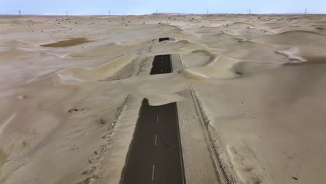Drone-shot-tilting-over-the-sandy-half-desert-road,-sunny-day-in-Dubai,-UAE
