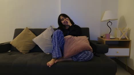 A-cute,-Asian-woman-in-her-pajamas-sitting-on-the-couch,-laughing