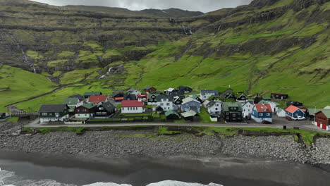 Tjørnuvík-village,-Faroe-Islands:-close-up-aerial-view-traveling-out-to-the-pretty-village,-with-the-ocean-and-mountains-in-the-background
