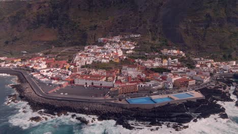 Garachico-fishing-village-in-the-Canary-Islands,-surrounded-by-its-sea-and-guarded-by-its-large-Catholic-church,-an-aerial-shot-from-a-drone-at-4K-60-Fps