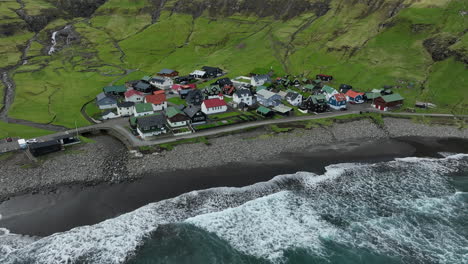 Tjørnuvík-village,-Faroe-Islands:-aerial-view-traveling-out-to-the-pretty-village,-with-the-ocean-and-mountains-in-the-background