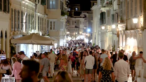 Corfu-Crowded-Street-at-Night-in-Old-City-of-Kerkyra-Greece,-Young-People-Walking-on-Alley-with-Shops-on-a-Summer-Night,-Real-Time-shot