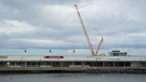 Burger-King-and-other-restaurants-with-a-huge-crane-in-the-background-at-the-bay-of-Ponta-Delgada,-San-Miguel-Island-of-the-Azores,-Portugal---July-2023