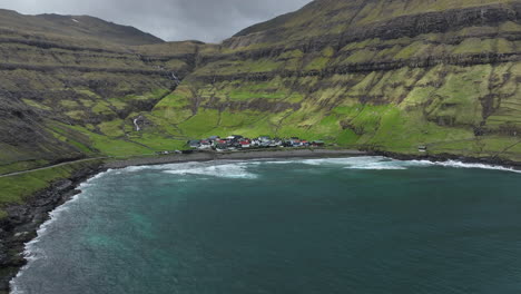 Tjørnuvík-village,-Faroe-Islands:-aerial-view-traveling-in-from-the-distance-and-towards-the-pretty-village,-with-the-ocean-and-mountains-in-the-background