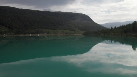 Impresionante-Vista-Aérea-De-Un-Lago-Verde-Azulado,-Turquesa,-Una-Carretera-Con-Algo-De-Tráfico-Es-Visible-En-La-Costa,-Noruega,-Hermosos-Reflejos-En-El-Agua,-Escandinavia